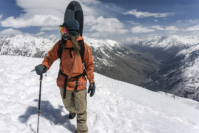 Man with ski pole carrying snowboard on snowcapped mountain during vacation — Stock Photo