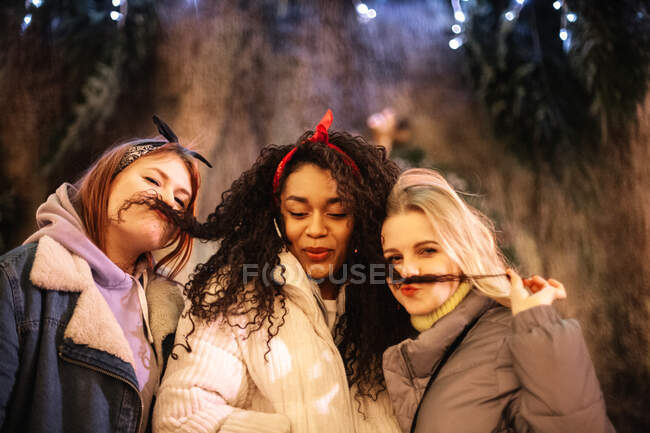 Jeunes femmes faisant de fausses moustaches avec des cheveux pendant Noël en ville — Photo de stock
