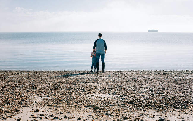 Father and daughter stood thoughtfully looking out to sea in the sun — Stock Photo