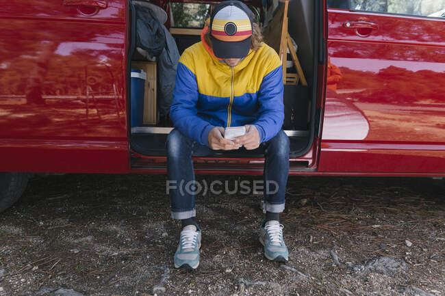 Мандрівник розслабився і використовує мобільний телефон, сидячи на своєму фургоні — стокове фото