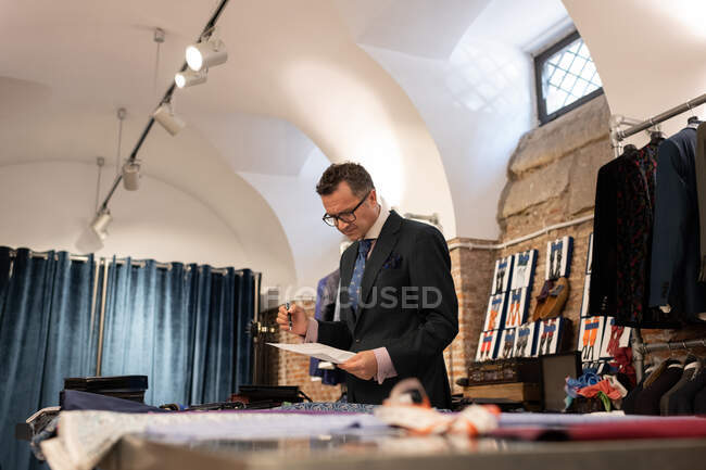 Maturo sarto maschio controllo schizzo su carta mentre si lavora in studio loft creativo — Foto stock