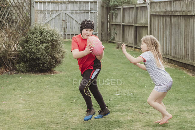 Young brother and sister playing with rugby ball in backyard — Stock Photo