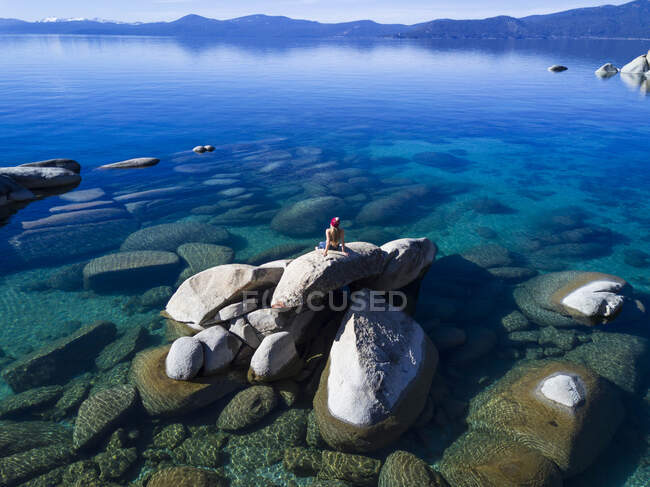 Jovem fêmea sentado na rocha no lago tahoe na tarde ensolarada — Fotografia de Stock