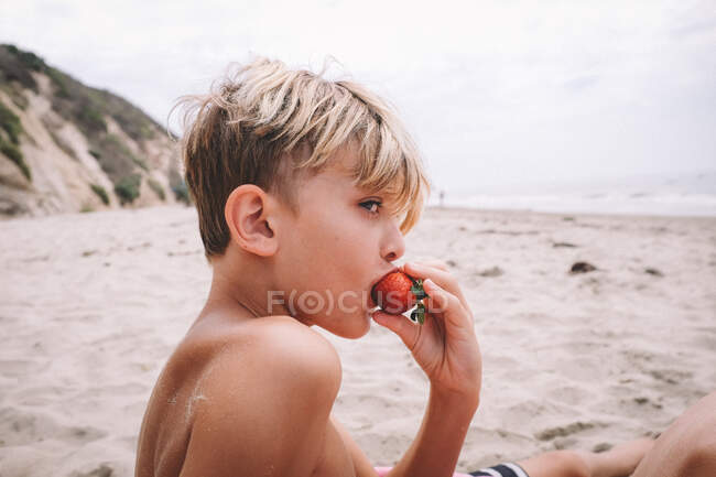 Rapaz a comer um morango numa praia de areia na Califórnia — Fotografia de Stock