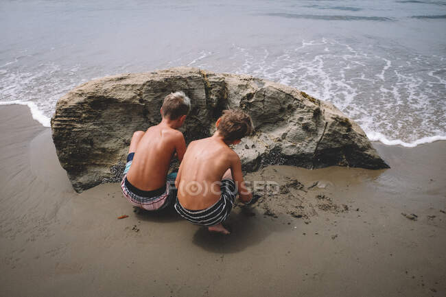 Dos hermanos en bañadores excavando arena en la playa - foto de stock