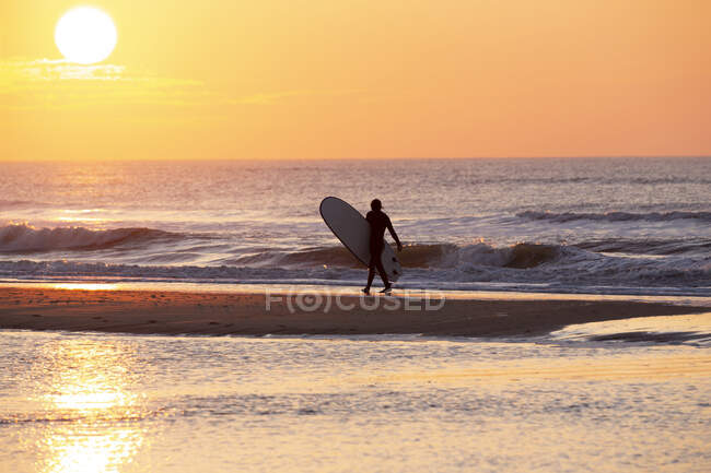 Un surfista che cammina lungo la spiaggia al tramonto — Foto stock