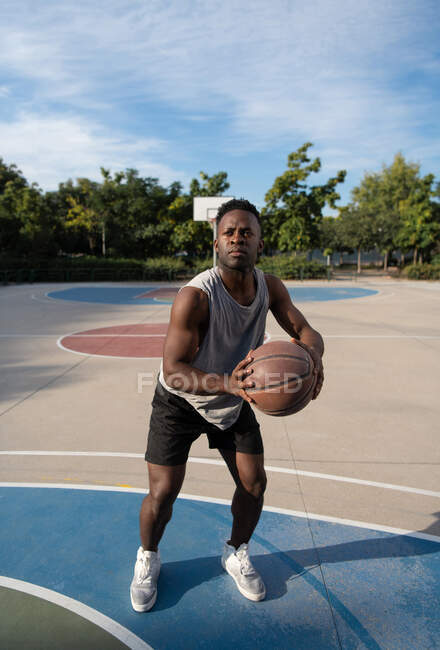 Strong ethnic athlete preparing to throw ball during basketball game on court — Stock Photo