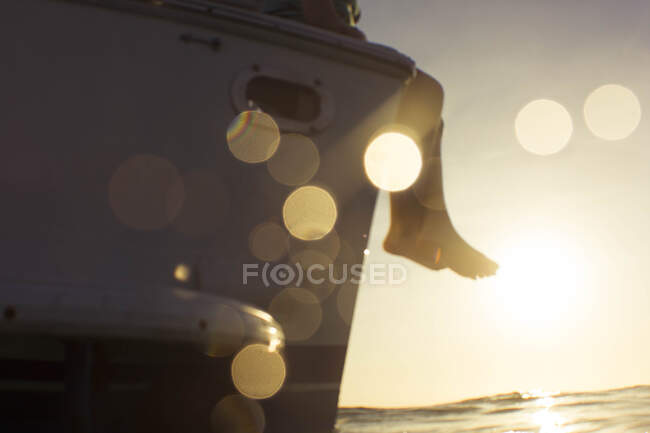 Feet hanging over boat at sunset — Stock Photo