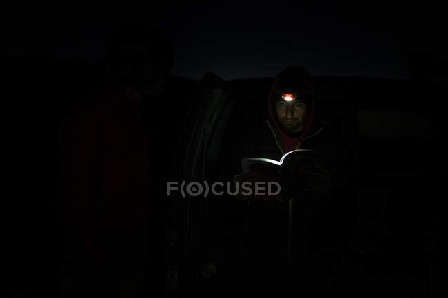 Hombre leyendo libro con luz de lámpara de cabeza durante la noche en el Parque Nacional Canyonlands - foto de stock