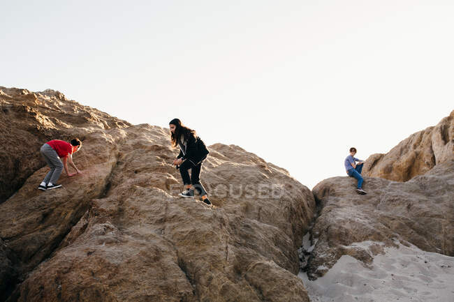 Três irmãos escalam por cima de uma enorme formação rochosa na praia — Fotografia de Stock