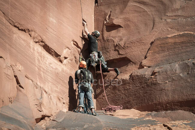 Amigos varones escalando formaciones rocosas en el Parque Nacional Canyonlands - foto de stock