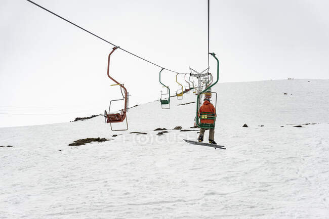 Вид сзади на человека, сидящего на лыжном подъемнике над снежным полем под ясным небом — стоковое фото
