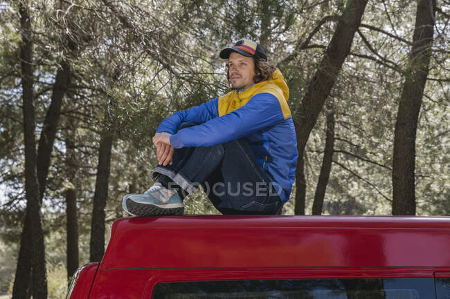 Hombre relajante y disfrutando de la calma mientras está sentado en el techo de la furgoneta. - foto de stock
