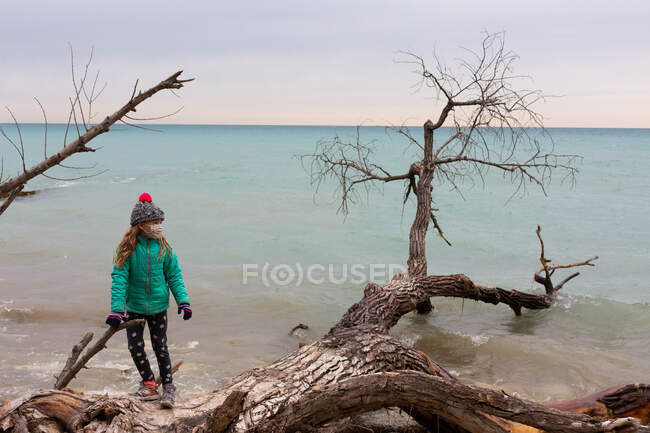 Vista lateral de un niño caminando en la orilla del lago en clima frío - foto de stock