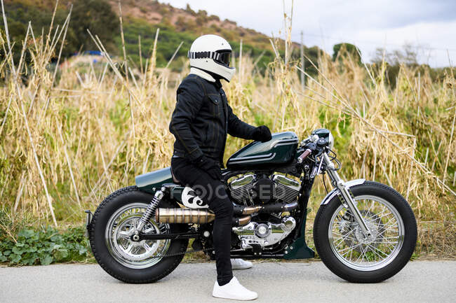 Вид збоку на мотоцикл, що стоїть на дорозі зі своїм власником — стокове фото
