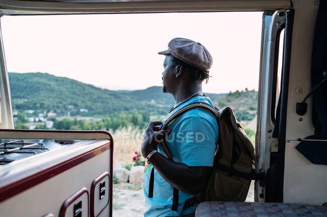 Afro americano homem com mochila olhando para uma paisagem sagacidade campista van — Fotografia de Stock