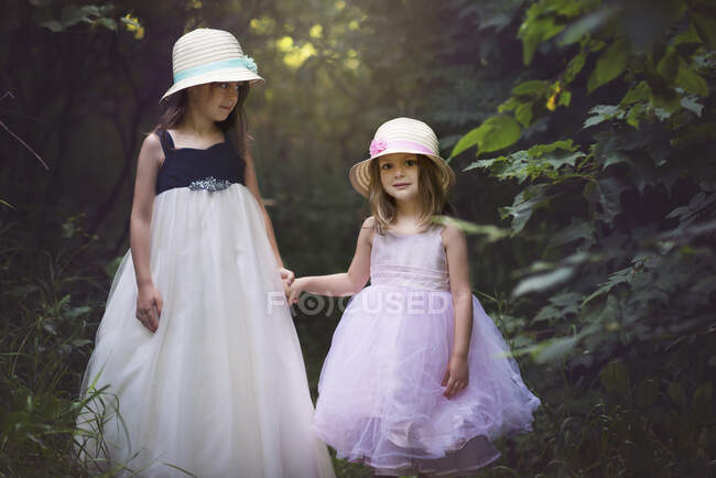 Dos niñas lindas en vestidos de Pascua tomados de la mano en el bosque. - foto de stock