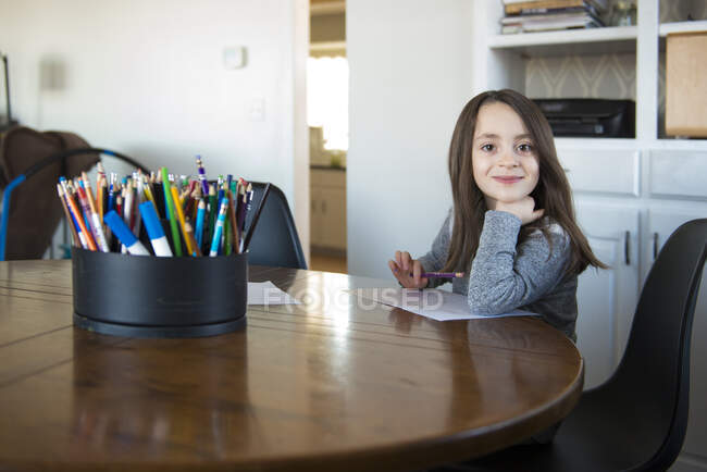 Little Girl Sitting at a table with paper and pencil. — Stock Photo