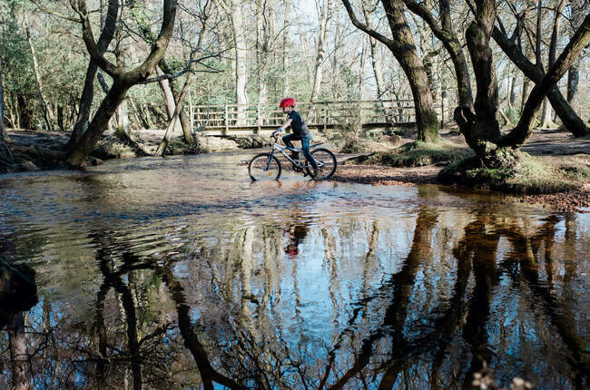 Giovane ragazzo in bicicletta attraverso un fiume da attraversare mentre mountain bike — Foto stock
