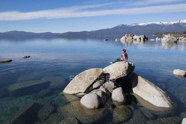 Young female sitting on rock in lake tahoe on sunny afternoon — Stock Photo