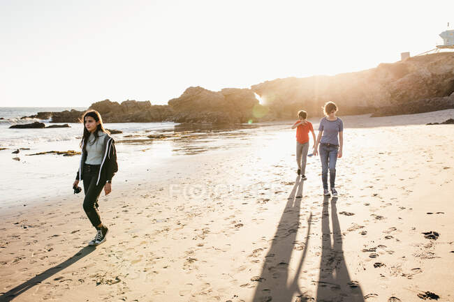 Trois frères et sœurs marchent sur la plage à marée basse au coucher du soleil — Photo de stock