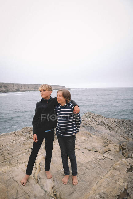 Best Friends pose  barefoot on a rocky cliff by the ocean — Stock Photo