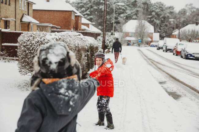 Fratelli che lanciano palle di neve in strada residenziale nella neve — Foto stock
