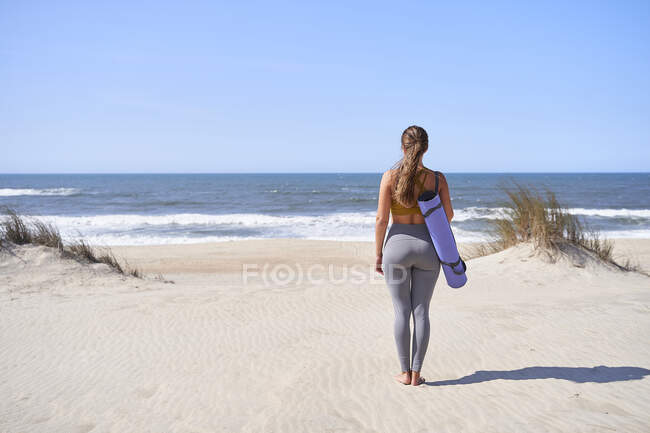 Chica frente al mar con una esterilla lista para hacer sus ejercicios de yoga por la mañana. concepto de libertad y vida saludable. - foto de stock