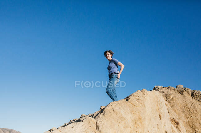 Adolescent fille se tient au-dessus un grand rocher avec bleu ciel entourant son — Photo de stock
