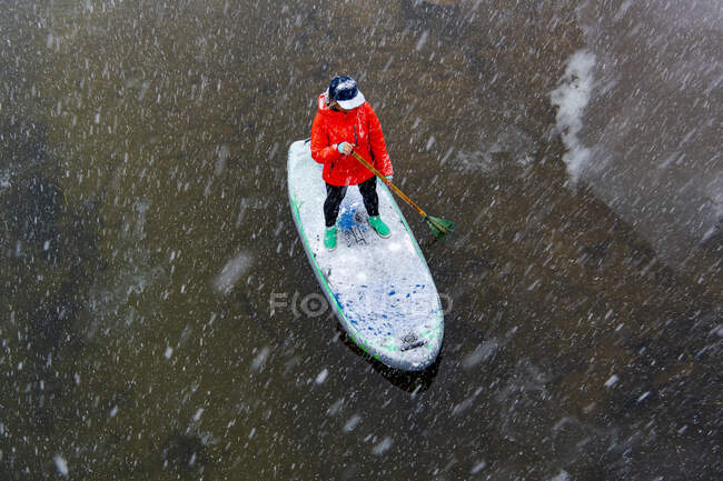 Высокий угол обзора женской гребли на реке во время снегопада — стоковое фото
