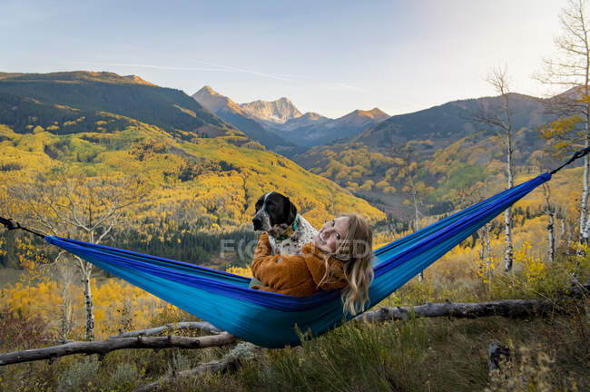 Happy young woman with dog relaxing on hammock in forest during vacation — Stock Photo