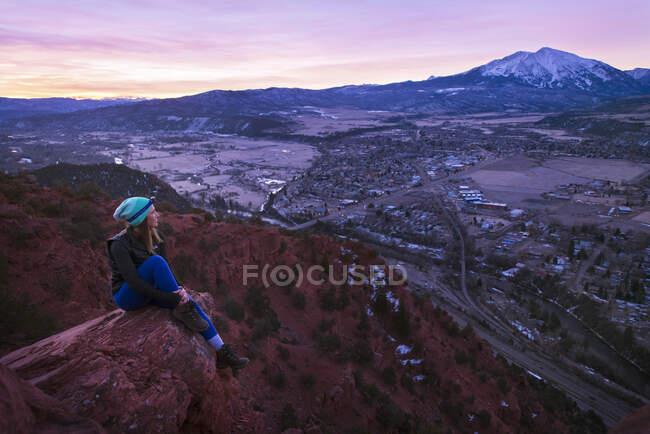 Jovem mulher com vista para a cidade da montanha ao pôr do sol — Fotografia de Stock