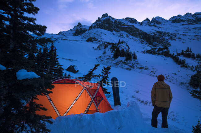 Jovem macho em pé fora da tenda no crepúsculo no inverno — Fotografia de Stock