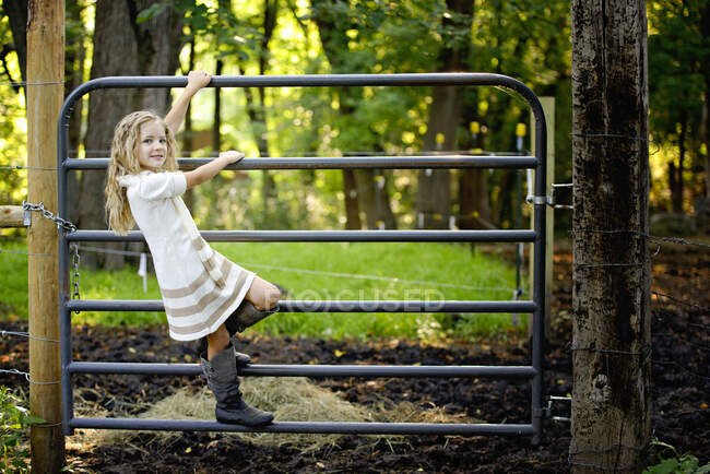 Menina loira escalando um portão na fazenda. — Fotografia de Stock