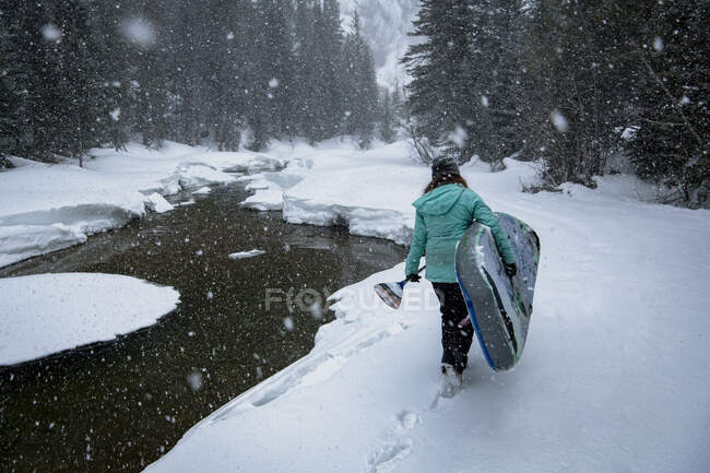 Visão traseira da mulher carregando paddleboard enquanto caminhava no campo de neve — Fotografia de Stock