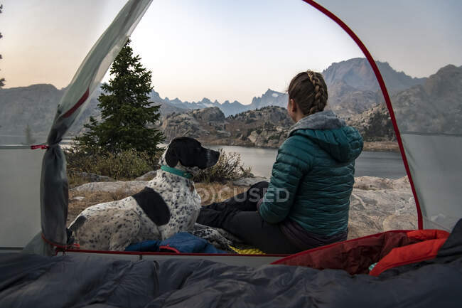 Woman sitting with dog by tent while camping during vacation — Stock Photo