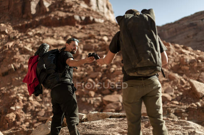 Man giving binoculars to friend while hiking on mountain at Canyonlands National Park — Stock Photo