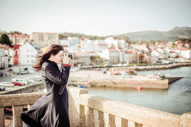 Brunette woman in dark coat taking photos from the top of a viewpoint — Stock Photo