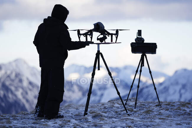 Silhouette of drone pilot with equipment on top of mountain in winter — Stock Photo