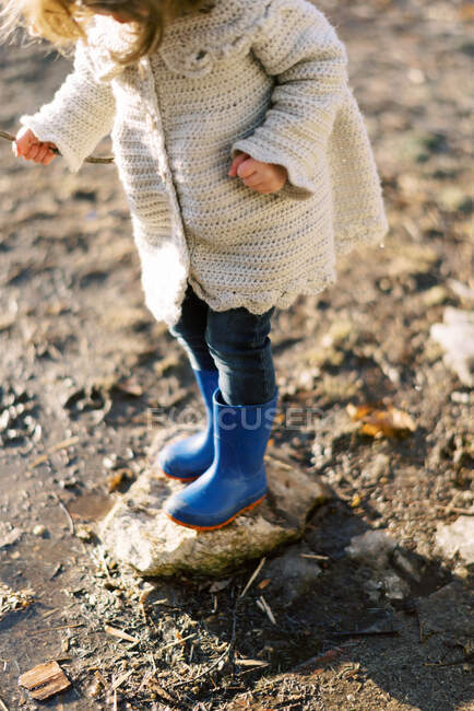 Маленькая девочка в домашней вязаной куртке и дождевых сапогах весной — стоковое фото