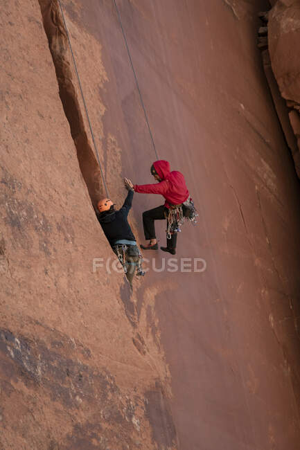 Hombres chocando los cinco mientras escalan el acantilado en el Parque Nacional Canyonlands - foto de stock