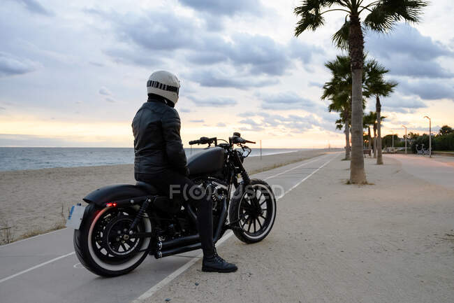 Vista trasera de una motocicleta de pie junto a una playa con su propietario solo - foto de stock
