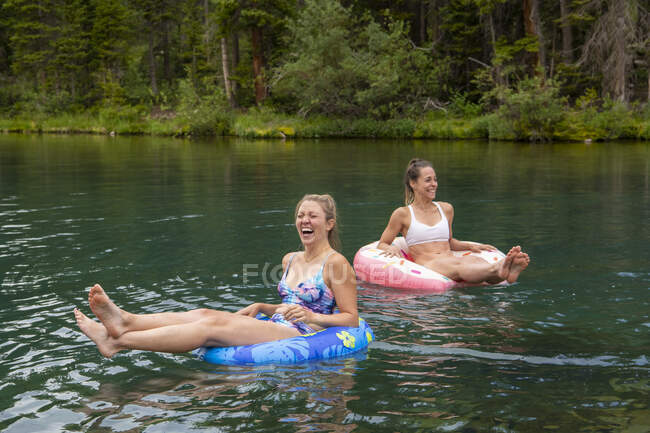 Cheerful female friends sitting on inflatable rings in lake — Stock Photo
