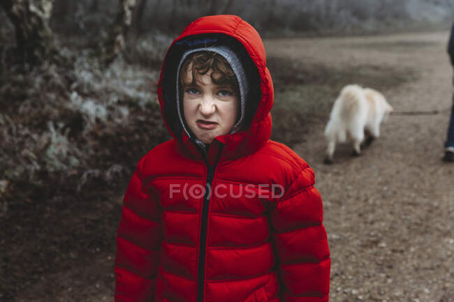 Menino de casaco vermelho de inverno olhando para a câmera e rosnando enroscando o nariz — Fotografia de Stock