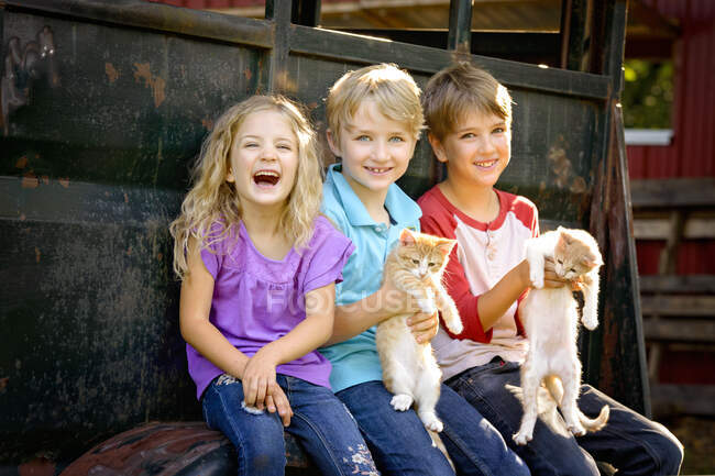 Drei glückliche blonde Kinder, die draußen mit Kätzchen spielen. — Stockfoto