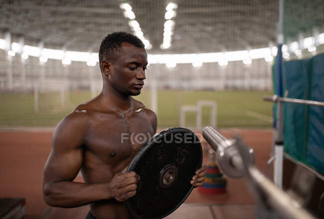 Strong African American man putting heavy weight on bar during training in stadium — Stock Photo