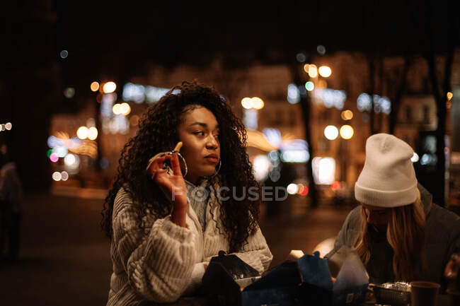 Jovens mulheres comendo comida de rua em pé à mesa na cidade à noite — Fotografia de Stock