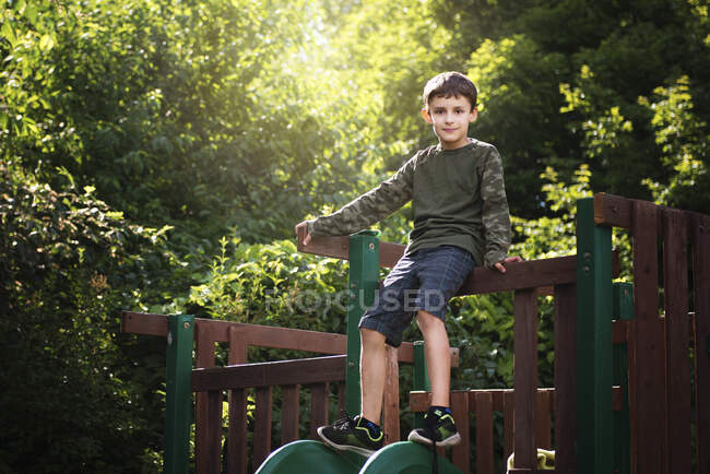 Menino em camuflagem e shorts sentado no topo de um slide. — Fotografia de Stock