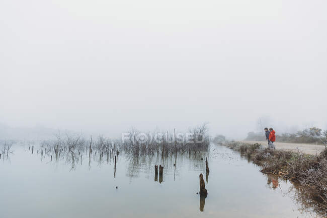 Dos hermanos de pie junto al lago en invierno contra el cielo nublado de niebla - foto de stock