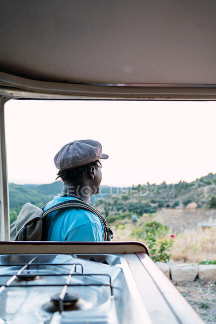 Afroamerikanischer Mann mit Rucksack blickt auf eine Landschaft mit Wohnmobil — Stockfoto